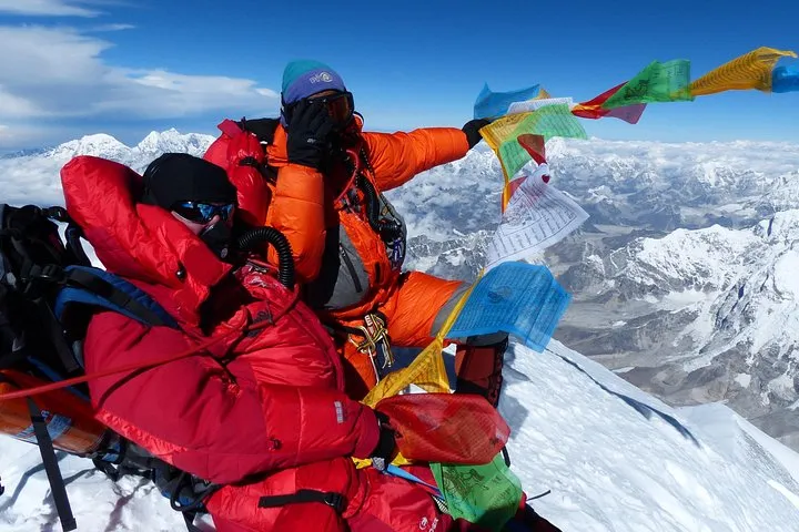 Climbers in red and orange down suits with prayer flags on the Everest summit on an Everest climbing tour, Nepal