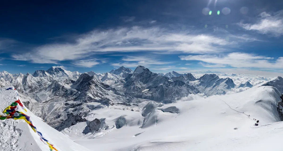 Prayer flags on the snow summit of Mera Peak above a sea of Himalayan peaks on one of the Everest climbing tours to a trekking peak